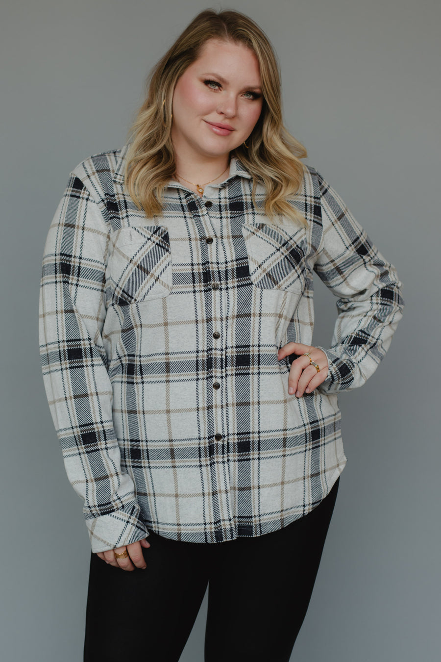 A woman with blonde hair wears the Panache Apparel Collection Black, Light Gray & Brown Plaid Button Up with long sleeves and black pants, standing in front of a plain gray background and smiling slightly.
