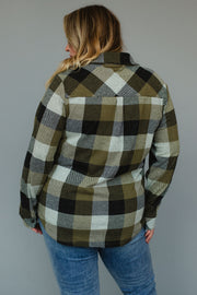 A person wearing the Olive & Black Plaid Button Up from Panache Apparel Collection with blue jeans is standing facing away from the camera against a plain gray background.