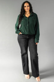 A person wearing a Hunter Green Super Soft Button Up long-sleeved shirt with front pockets and black jeans.