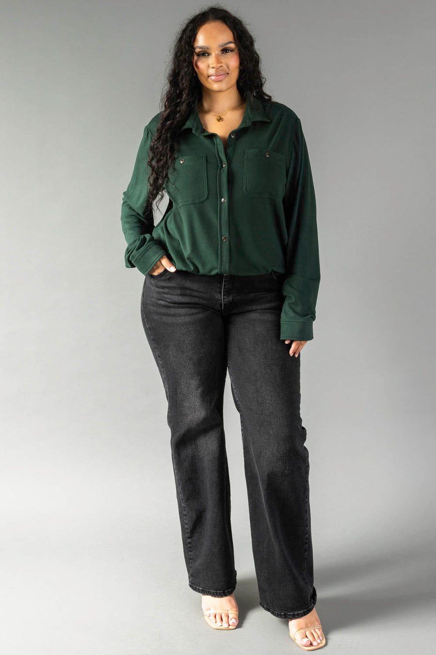 A person wearing a Hunter Green Super Soft Button Up long-sleeved shirt with front pockets and black jeans.