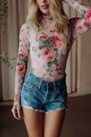 A woman with long blonde hair wears the Panache Apparel Collection Pink & Green Floral Mesh Top with high-waisted denim shorts and layered gold necklaces. Her face is partially out of frame.