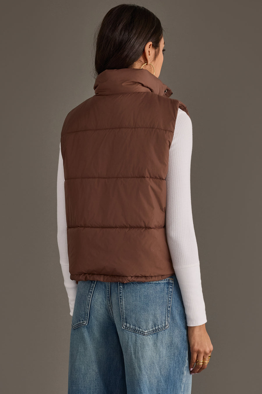 A woman is seen from behind, modeling the Panache Apparel Collection Brown Vest layered over a white long-sleeve top and blue jeans, set against a plain grey background.