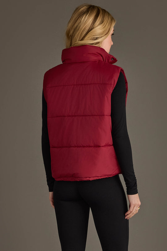 A person with long blonde hair is seen from the back against a plain background wearing the Panache Apparel Collection Burgundy Vest over a black long-sleeve shirt and black leggings.