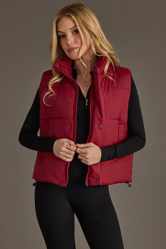 A woman models the Panache Apparel Collection Burgundy Vest over a black long-sleeve top and black pants, standing against a plain gray background with a neutral expression.