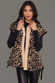 A woman wearing the Panache Apparel Collection’s Tan & Brown Leopard Fleece Vest over a black long-sleeve top and black pants stands against a plain grey background, looking at the camera and holding the vest’s collar.