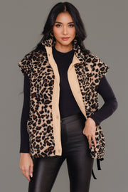 A woman stands confidently against a plain gray background, wearing the Panache Apparel Collection Tan & Brown Leopard Fleece Vest over a black turtleneck sweater and black leather pants.