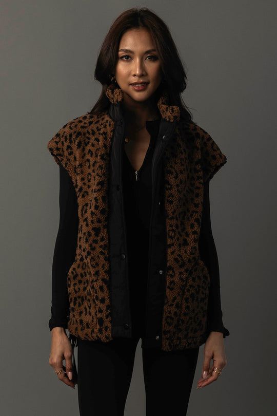 A woman models the Panache Apparel Collection Brown & Black Leopard Fleece Vest over a black long-sleeve top, standing against a plain dark background and looking at the camera with a slight smile.