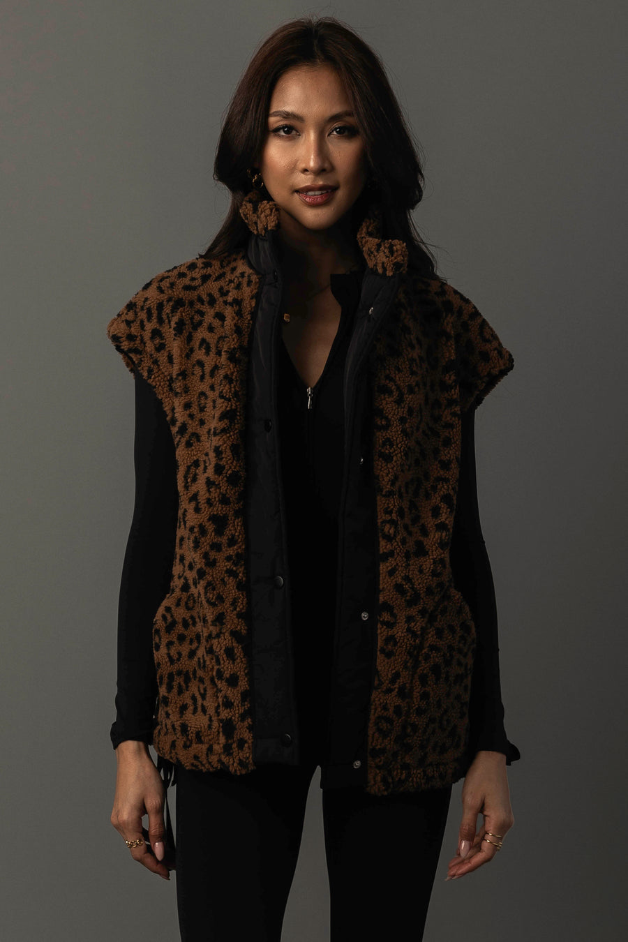 A woman models the Panache Apparel Collection Brown & Black Leopard Fleece Vest over a black long-sleeve top, standing against a plain dark background and looking at the camera with a slight smile.
