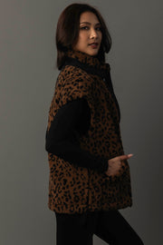 A woman with long dark hair stands sideways against a plain gray background, wearing the Panache Apparel Collection Brown & Black Leopard Fleece Vest over a black long-sleeve top, with her left hand in the vest pocket.