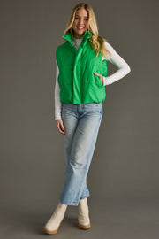 Full-length view of woman wearing Bright Green World Traveler puffer vest styled with jeans and boots.