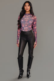 A woman stands against a gray background wearing the Panache Apparel Collection’s Reddish Brown Floral Mesh Top, paired with high-waisted black pants and knee-high black boots. She has long, wavy dark hair and a neutral expression.