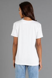 A woman with long dark hair, wearing the Panache Apparel Collection’s Here For The Boos Tee, a plain white short-sleeve t-shirt, and light blue jeans, stands facing away from the camera against a plain gray background.