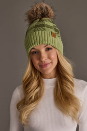 A woman with long blonde hair smiles at the camera against a plain background, wearing a Panache Apparel Collection Light Green & Olive Plaid Knit Pom Hat and a white ribbed sweater.