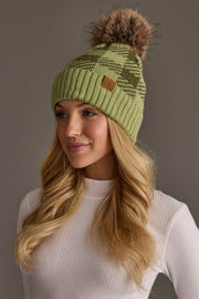 A woman with long blonde hair wears the Panache Apparel Collection’s Light Green & Olive Plaid Knit Pom Hat, featuring a brown faux fur pom-pom, along with a white ribbed long-sleeve top as she looks slightly to the side against a plain gray background.