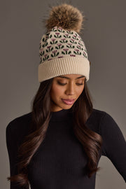 A woman wearing the Panache Apparel Collection Cream Small Floral Pattern Knit Pom Hat and a black ribbed long-sleeve top stands against a plain gray background.