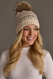 A smiling woman with long blonde hair wears the Panache Apparel Collection Cream & Pink Floral Pattern Pom Hat and a white ribbed long-sleeve top, posing against a plain gray background.