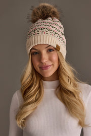 A woman with long blonde hair wears the Panache Apparel Collection Cream & Pink Floral Pattern Pom Hat, featuring a cute pom-pom and subtle pink and green floral designs. She is styled in a white ribbed turtleneck and smiles gently against a plain background.