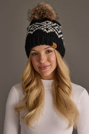 A woman with long blonde hair wears a white ribbed sweater and the Panache Apparel Collection Black & White Patterned Pom Hat, smiling softly against a neutral background.