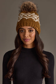 A woman with long, wavy hair wears the Panache Apparel Collection Camel & White Patterned Pom Hat and a black ribbed long-sleeve top, posing against a plain, neutral background.