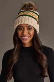 A woman smiles while wearing the Panache Apparel Collection’s Cream, Green & Gold Patterned Pom Hat and a black long-sleeve top, set against a plain gray background.