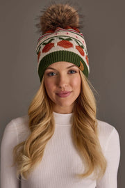 A woman with long blonde hair wears a white ribbed sweater and the Panache Apparel Collection’s Olive, Cream, Rust & Pink Patterned Pom Hat, a colorful knit beanie adorned with a pom-pom,while standing against a plain gray background.
