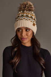 Model wearing the Panache Apparel Collection’s Beige, Mustard & Green Patterned Pom Hat, a knit beanie featuring a geometric design and a fur pom-pom, paired with a black ribbed turtleneck, gazing slightly to the side against a plain gray background.