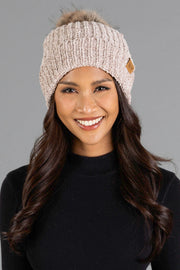 A woman with long dark hair smiles while wearing the Panache Apparel Collection’s Taupe Chenille Pom Hat and a black sweater, standing in front of a plain gray background.