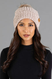 A woman with long dark hair is wearing the Taupe Chenille Pom Hat by Panache Apparel Collection and a black top, posing against a plain gray background.