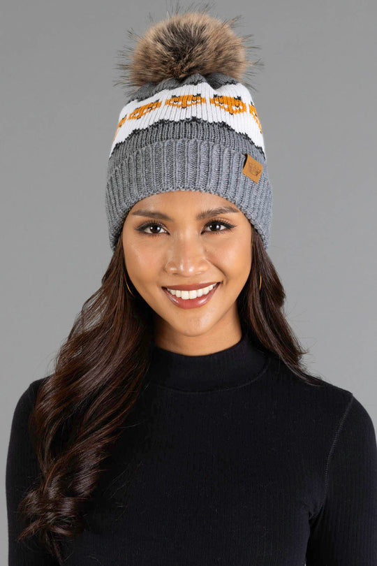 A woman smiles while wearing the Panache Apparel Collection’s Gray with Orange Fox Pattern Knit Pom Hat, styled with a black ribbed long-sleeve top against a plain gray background.