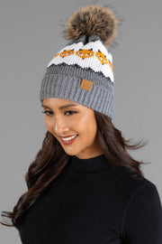 A woman with long dark hair smiles while wearing the Panache Apparel Collection Gray with Orange Fox Pattern Knit Pom Hat, which features a gray knit design, playful pom-pom, white and orange fox motifs, and a leather tag. She pairs it with a black top against a gray background.