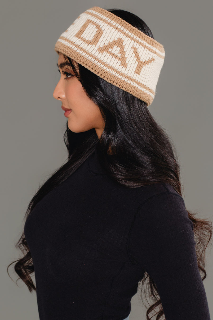 A woman with long black hair, shown in profile against a gray background, wears a black top and the Panache Apparel Collection’s Beige & Tan Game Day Knit Headband featuring “DAY” in beige letters.
