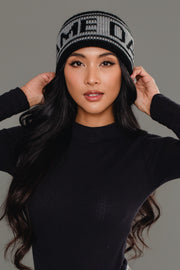 A woman with long black hair wears the Panache Apparel Collection Black & Gray Game Day Knit Headband and a black long-sleeve top, posing with her hands touching the sides of the headband against a plain gray background.