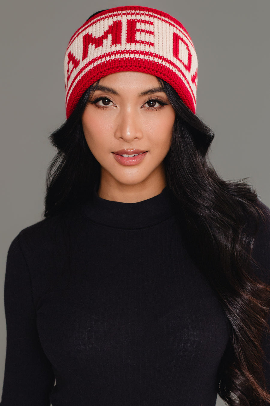 A woman with long, wavy black hair wears the Red & Beige Game Day Knit Headband by Panache Apparel Collection. She has on a black ribbed top and looks directly at the camera with a soft smile.