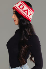A woman in profile wears the Panache Apparel Collection Red & Beige Game Day Knit Headband, styled with long wavy dark hair, a black long-sleeve top, and light blue jeans against a plain gray background.