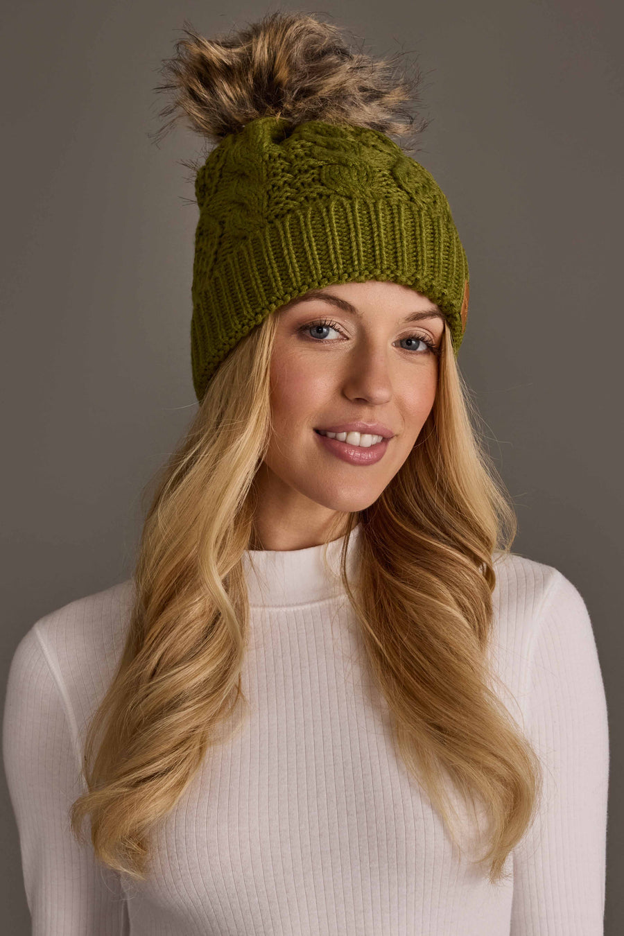 Woman wearing an olive green Olive Green Cable Knit Pom Hat with a faux fur pom.