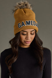 Model styling Panache Apparel’s camel Game Day knit beanie with gray text and a cozy ribbed cuff.