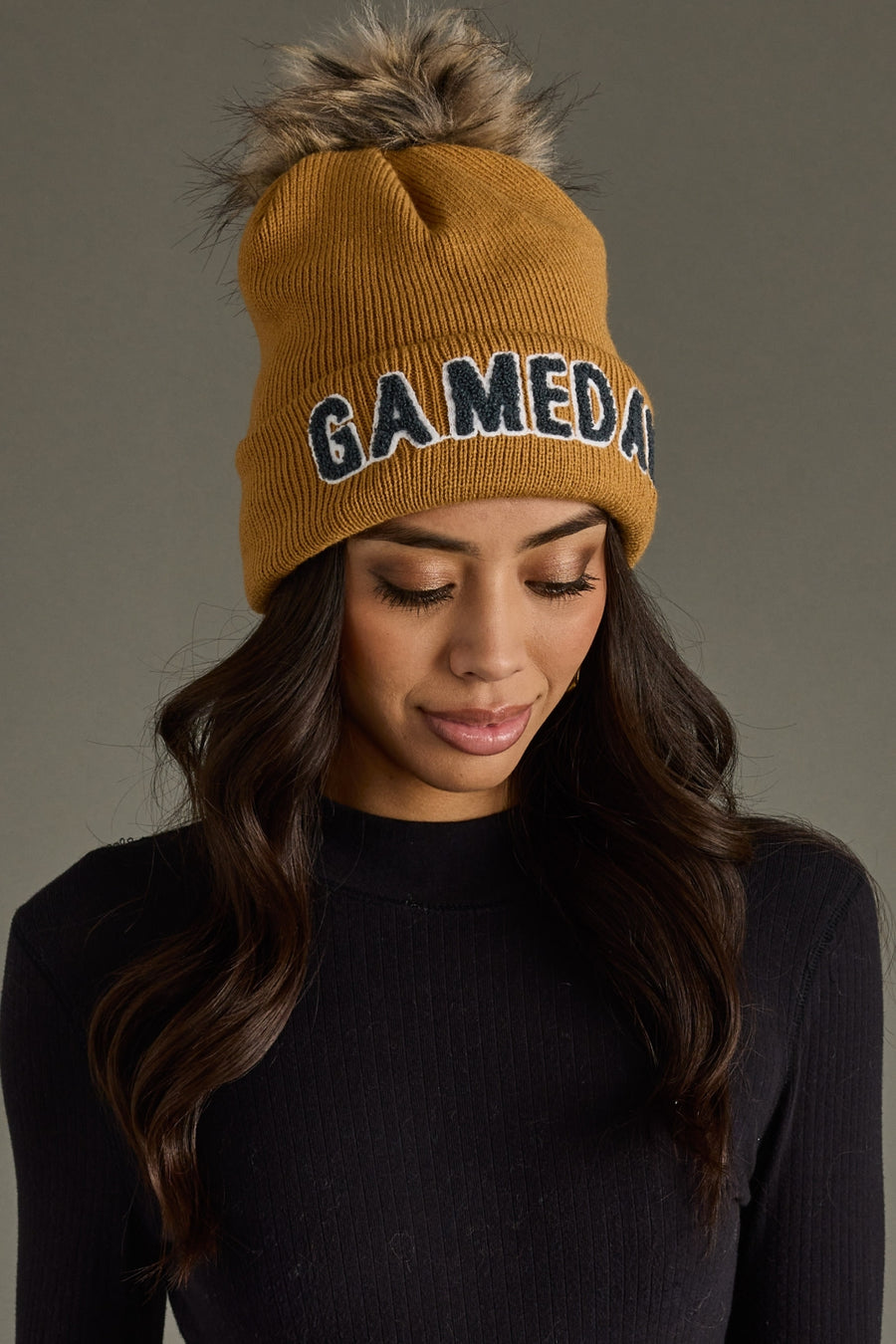 Model styling Panache Apparel’s camel Game Day knit beanie with gray text and a cozy ribbed cuff.