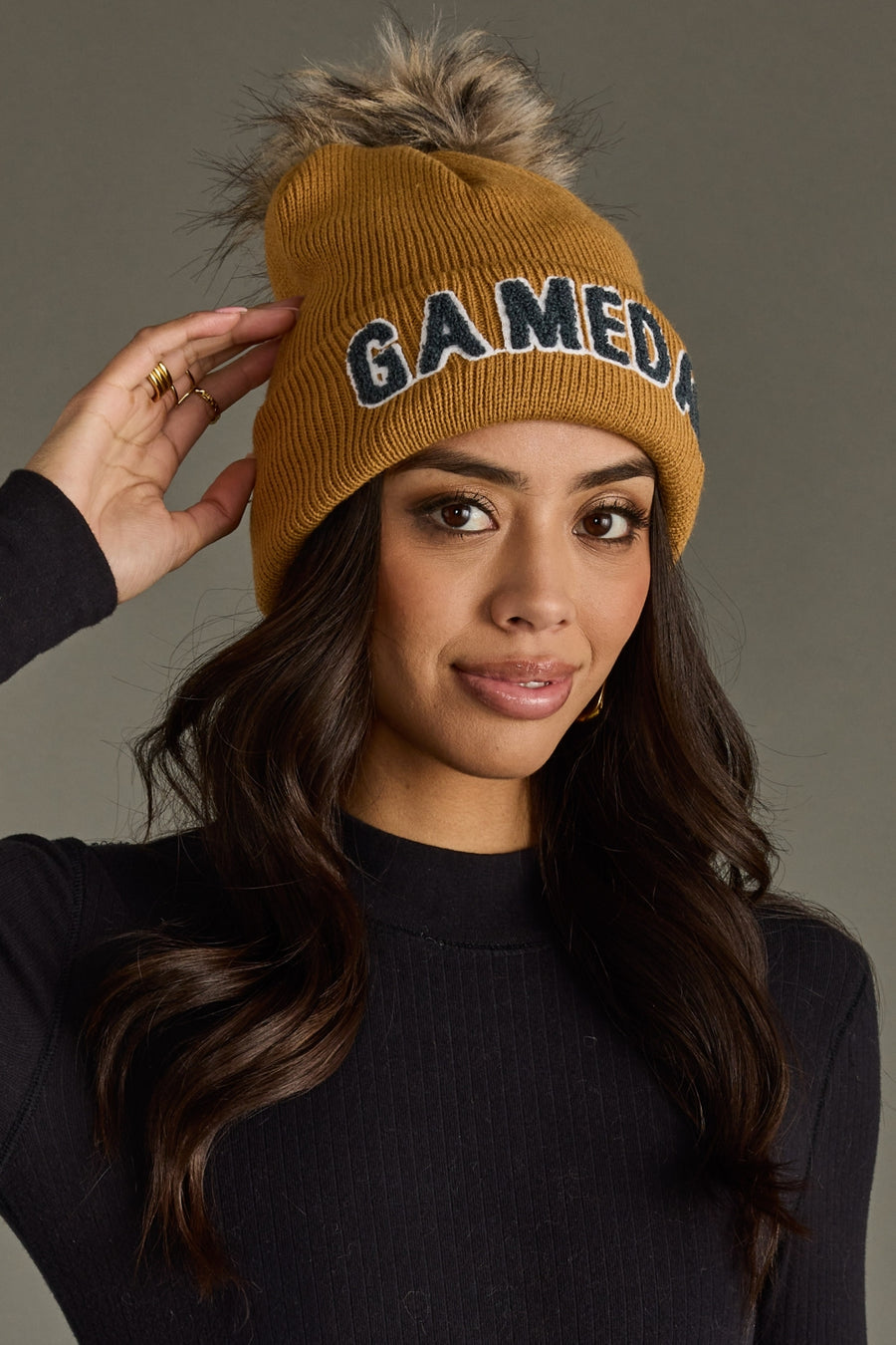 Close-up of woman adjusting Panache Apparel’s camel and gray Game Day pom hat with a soft faux fur topper.