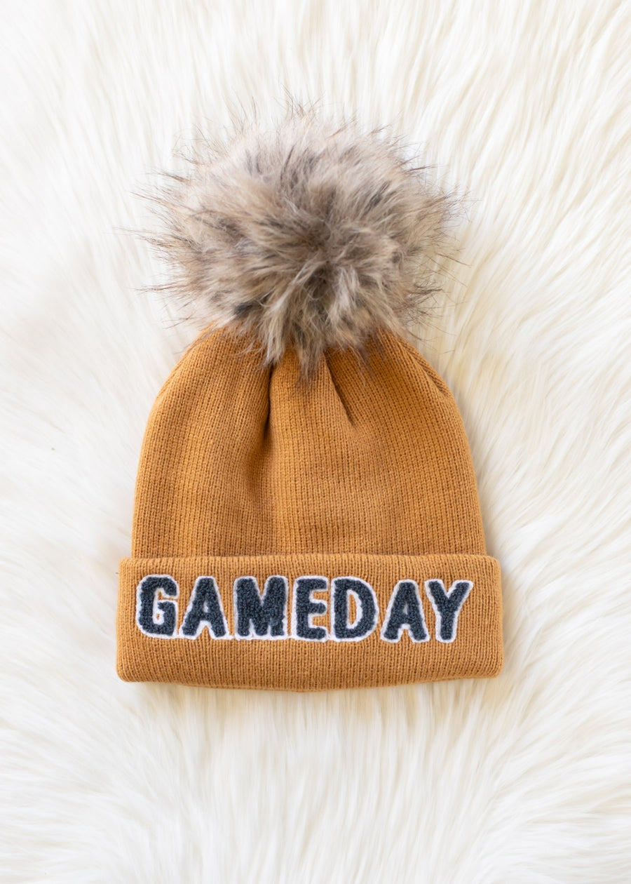 Flat lay of Panache Apparel’s camel and gray Game Day knit hat featuring bold text and a faux fur pom.