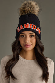 Woman with long dark hair wearing Panache Apparel’s black and orange Game Day pom hat with bold lettering and a faux fur pom.