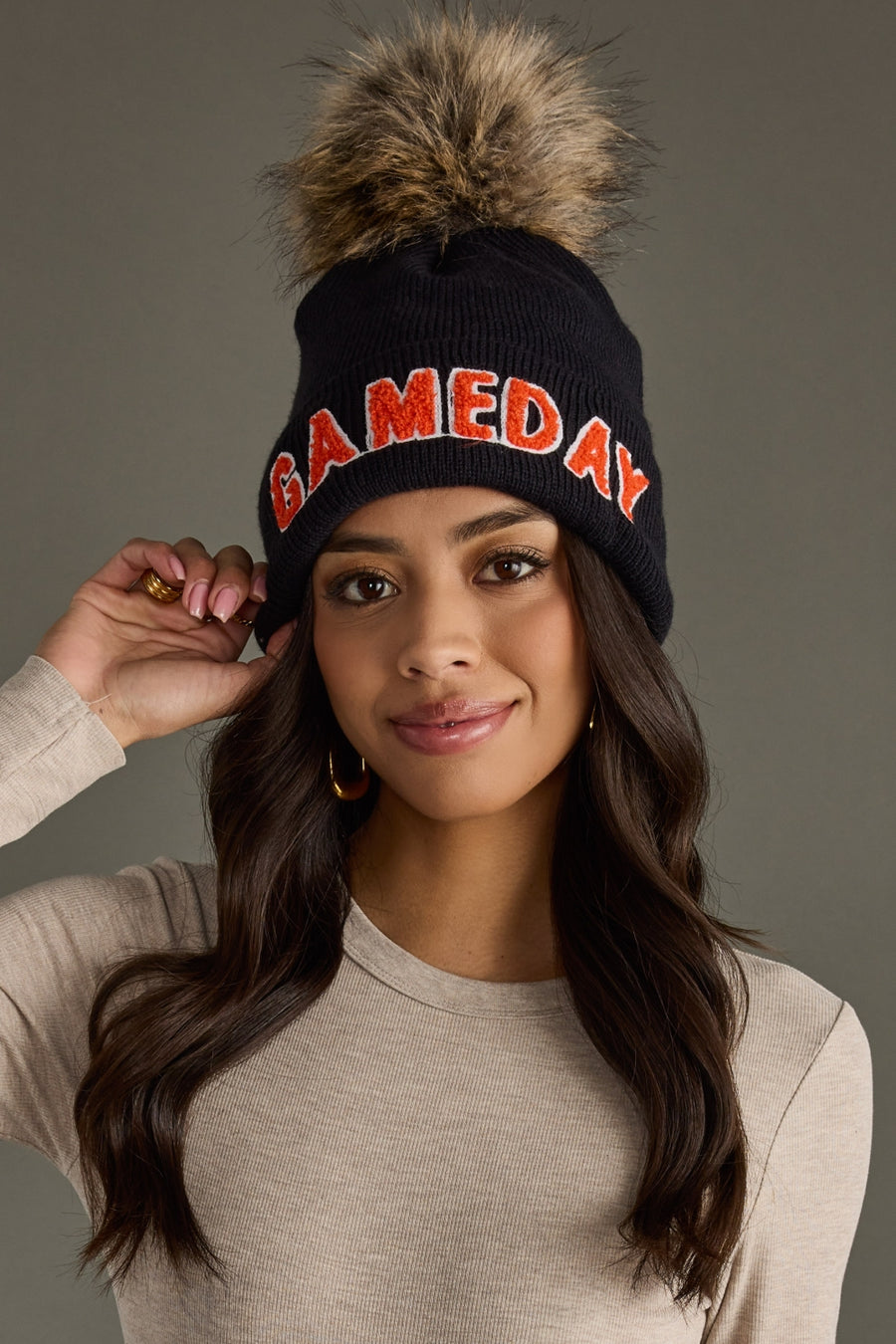 Model wearing Panache Apparel’s black knit Game Day beanie with orange text, ribbed cuff, and faux fur topper.