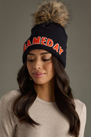 Woman styling Panache Apparel’s black and orange Game Day pom hat in a cozy winter look.