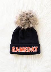 Flat lay of Panache Apparel’s black Game Day knit hat featuring orange lettering and a faux fur pom.