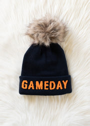 Product flat lay of Panache Apparel’s navy knit Game Day hat with orange text and a faux fur pom.