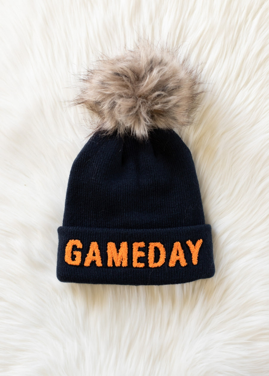 Product flat lay of Panache Apparel’s navy knit Game Day hat with orange text and a faux fur pom.