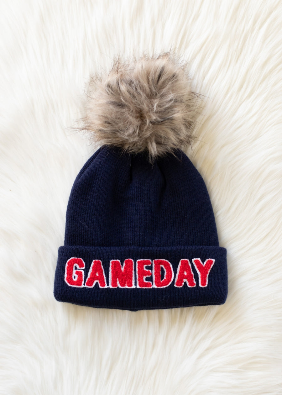 Flat lay of Panache Apparel’s navy and red Game Day winter hat featuring a folded cuff and faux fur topper.