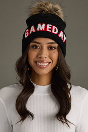 Smiling woman wearing Panache Apparel’s black Game Day pom hat with white and red lettering, a ribbed cuff, and faux fur pom.