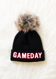 Flat lay of Panache Apparel’s black, white, and red Game Day pom hat with bold lettering and a faux fur topper.