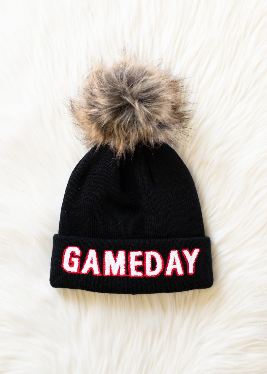 Flat lay of Panache Apparel’s black, white, and red Game Day pom hat with bold lettering and a faux fur topper.