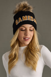 Model showcasing Panache Apparel’s black knit Game Day beanie with tan text, a ribbed cuff, and cozy pom detail.